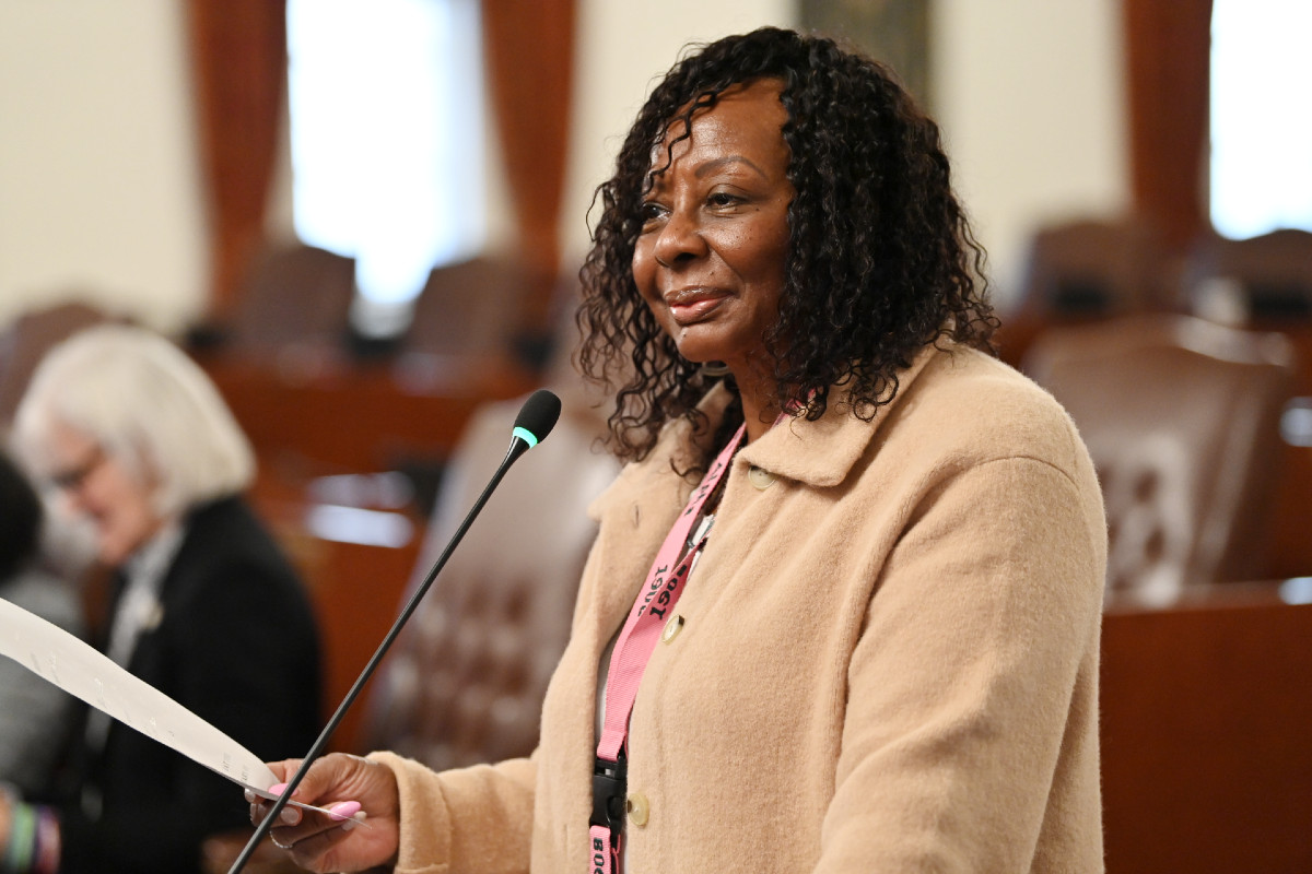 Senator Hunter smiles while holding a piece of paper, standing in the Senate chamber.