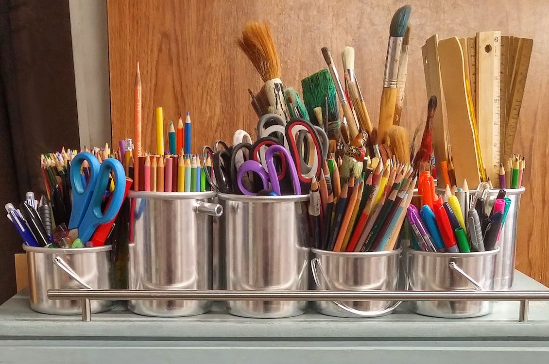 Metal cups of school supplies including scissors, colored pencils, paint brushes and rules.