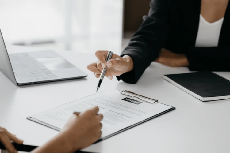 A hands-only photo of two people across a desk using pens to point to a resume.